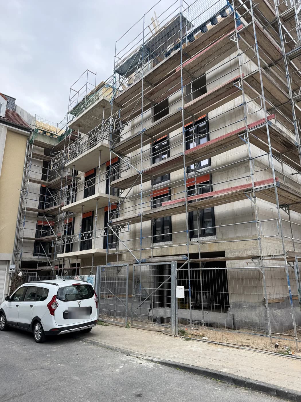 Mehrfamilienhaus im Bau mit Gerüst und eingebauten dunklen Fenstern
